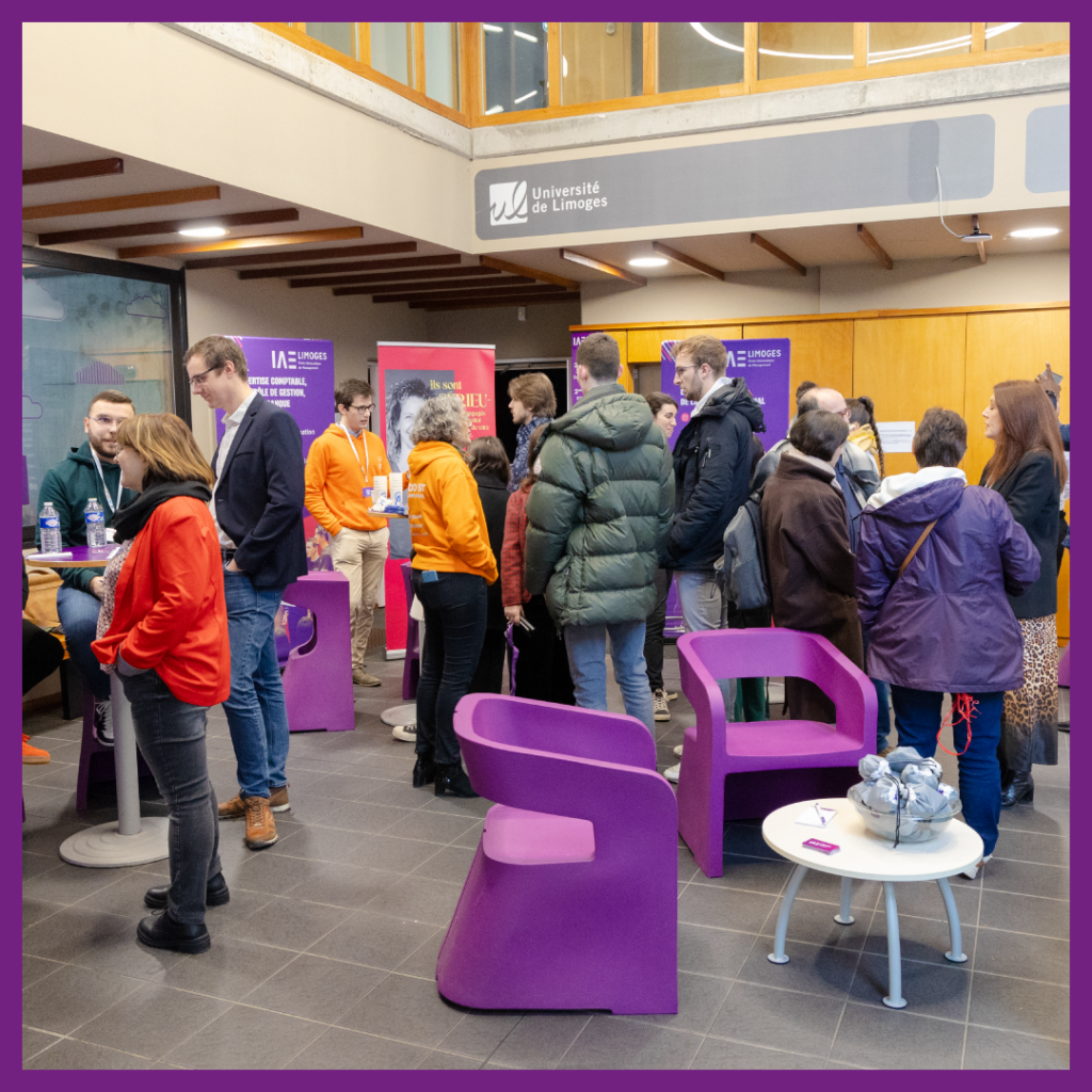 Photo prise lors des Journées Portes Ouvertes 2024 de l'IAE Limoges. L'image montre un hall animé où des visiteurs échangent avec des étudiants et des membres du personnel, vêtus de gilets orange, autour de stands d'information. Des éléments visuels aux couleurs de l'Université de Limoges et de l'IAE Limoges sont visibles en arrière-plan, ainsi que des fauteuils violets et une table basse au premier plan.