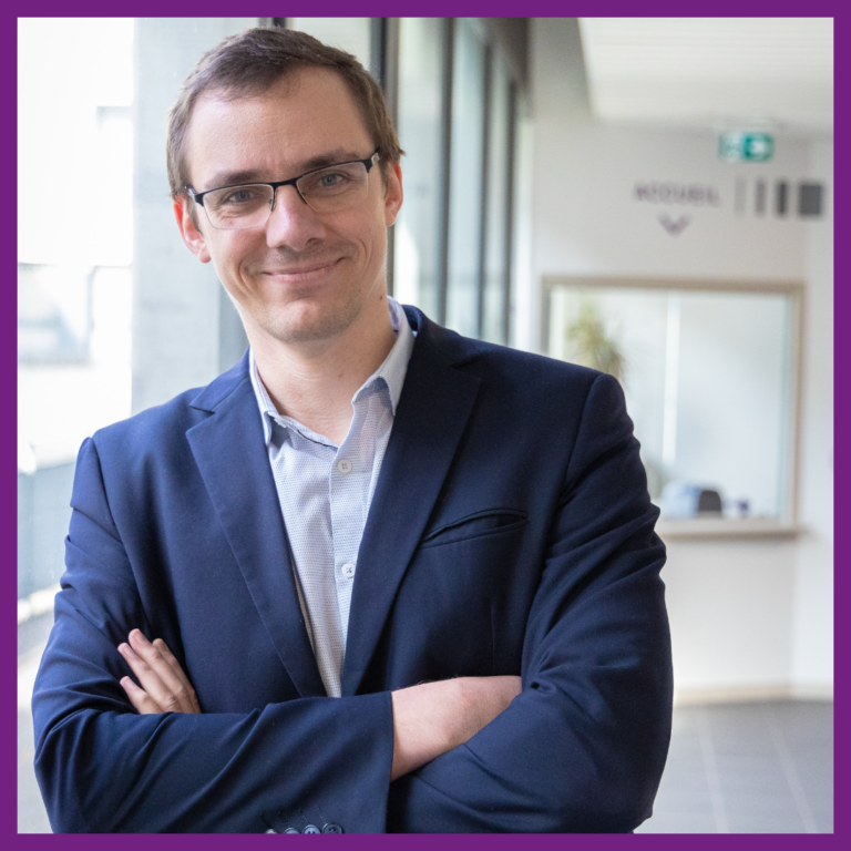 Portrait de Gauthier CASTERAN, nouveau directeur de l’IAE Limoges. Il porte un costume bleu et une chemise claire. Il est souriant. L’arrière-plan montre un couloir lumineux au sein de l'École.