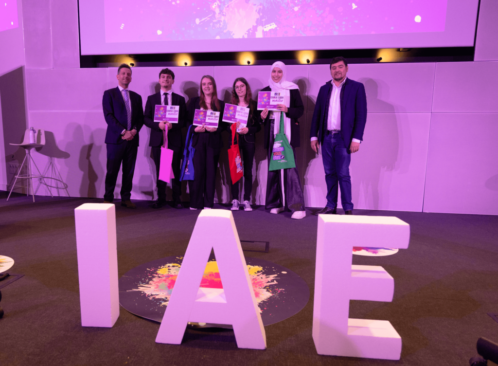 Remise de prix lors de la finale 2025 des Ateliers de l’innovation. Lauréats et membres du jury sont alignés sur scène, tenant diplômes et trophées, devant de grandes lettres formant « IAE ». L'événement met en lumière les projets innovants des étudiants.