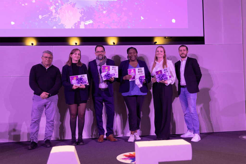 Remise de prix lors de la finale 2025 des Ateliers de l’innovation. Lauréats et membres du jury sont alignés sur scène, tenant diplômes et trophées, devant de grandes lettres formant « IAE ». L'événement met en lumière les projets innovants des étudiants.