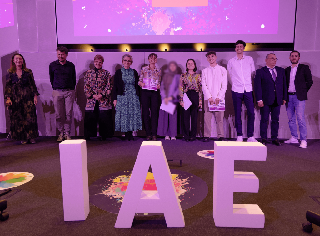 Remise de prix lors de la finale 2025 des Ateliers de l’innovation. Lauréats et membres du jury sont alignés sur scène, tenant diplômes et trophées, devant de grandes lettres formant « IAE ». L'événement met en lumière les projets innovants des étudiants.