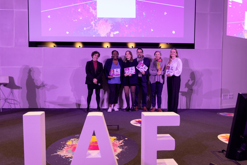 Remise de prix lors de la finale 2025 des Ateliers de l’innovation. Lauréats et membres du jury sont alignés sur scène, tenant diplômes et trophées, devant de grandes lettres formant « IAE ». L'événement met en lumière les projets innovants des étudiants.
