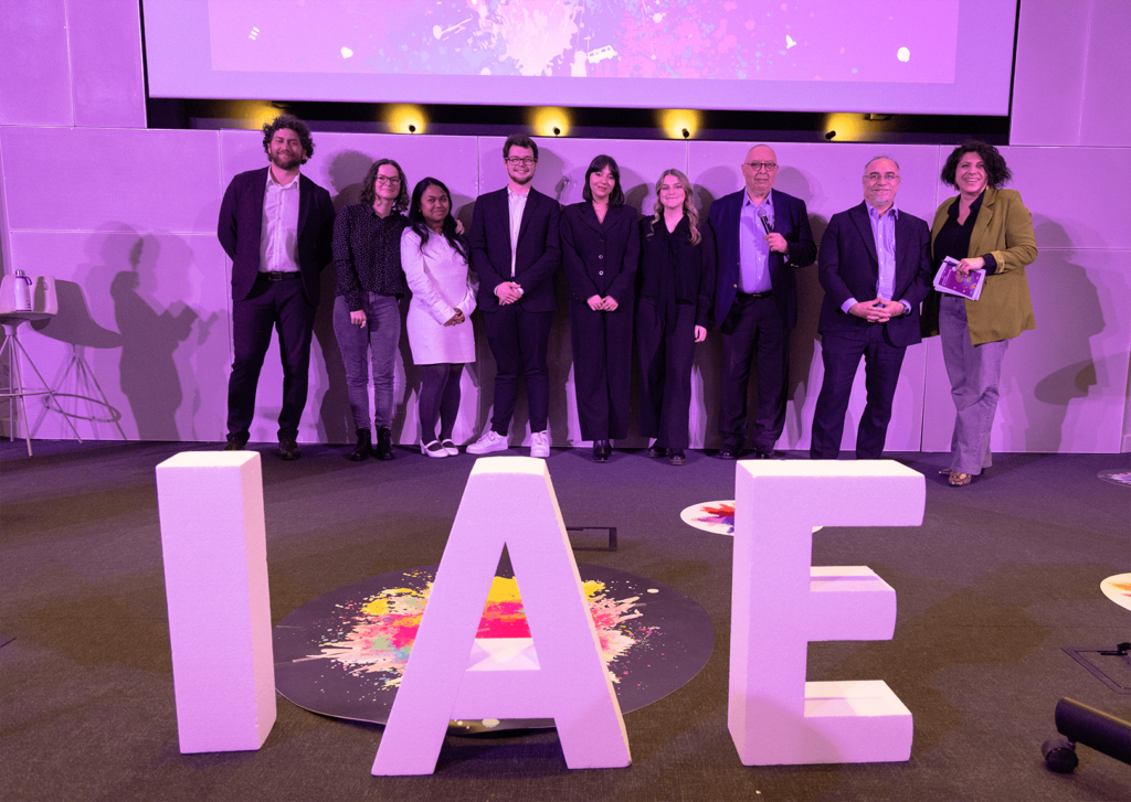 Remise de prix lors de la finale 2025 des Ateliers de l’innovation. Lauréats et membres du jury sont alignés sur scène, tenant diplômes et trophées, devant de grandes lettres formant « IAE ». L'événement met en lumière les projets innovants des étudiants.
